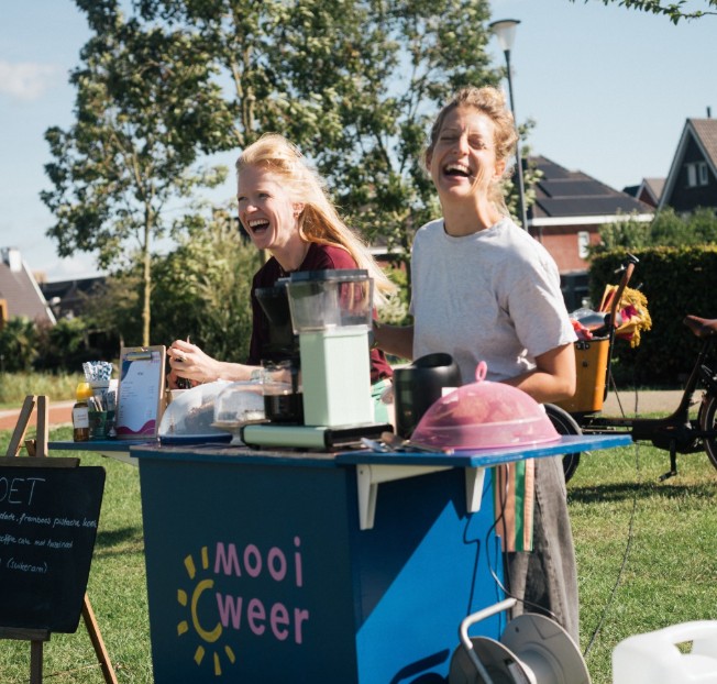 Simone en Anne lachend achter de Mooi Weer koffiekar